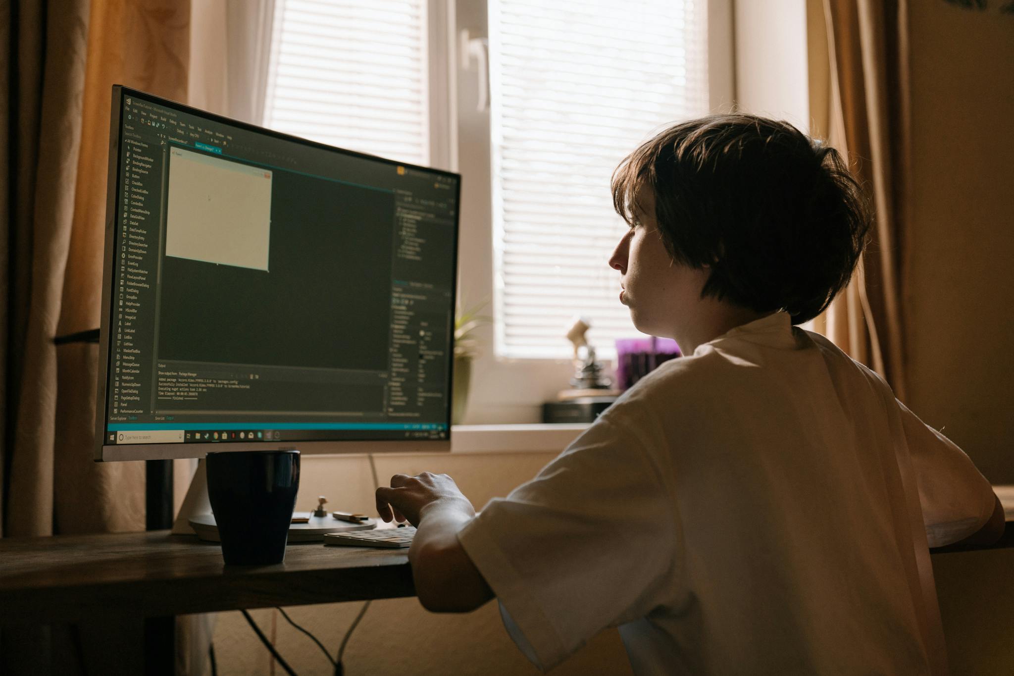 A young boy focused on programming at a desk with a large monitor in a softly lit room.