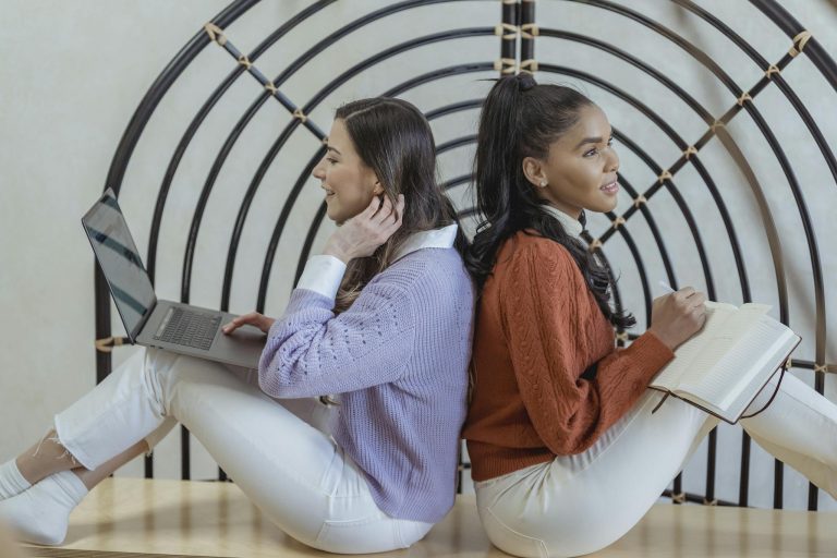 Two women working and studying together with laptop and notebook, symbolizing teamwork and creativity.
