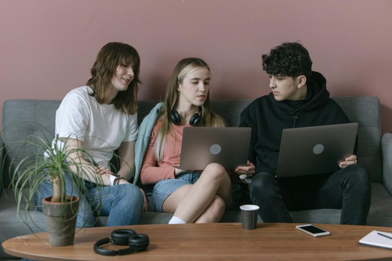 Young adults collaborating with laptops on a sofa in a casual office environment.